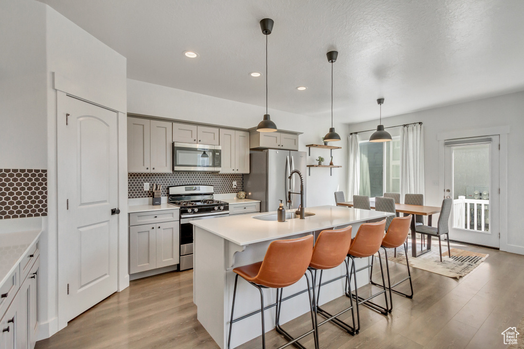 Kitchen with tasteful backsplash, a center island with sink, stainless steel appliances, light hardwood / wood-style flooring, and hanging light fixtures