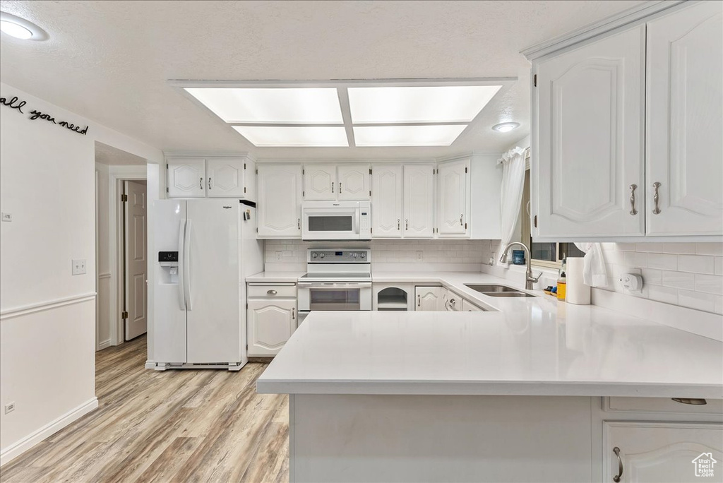 Kitchen with sink, white appliances, tasteful backsplash, and light wood-type flooring