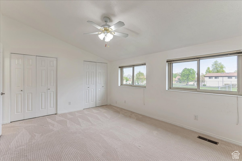 Unfurnished bedroom with light colored carpet, ceiling fan, vaulted ceiling, and multiple closets