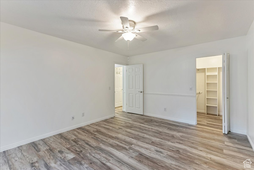 Unfurnished bedroom with a walk in closet, ceiling fan, a closet, and light hardwood / wood-style flooring