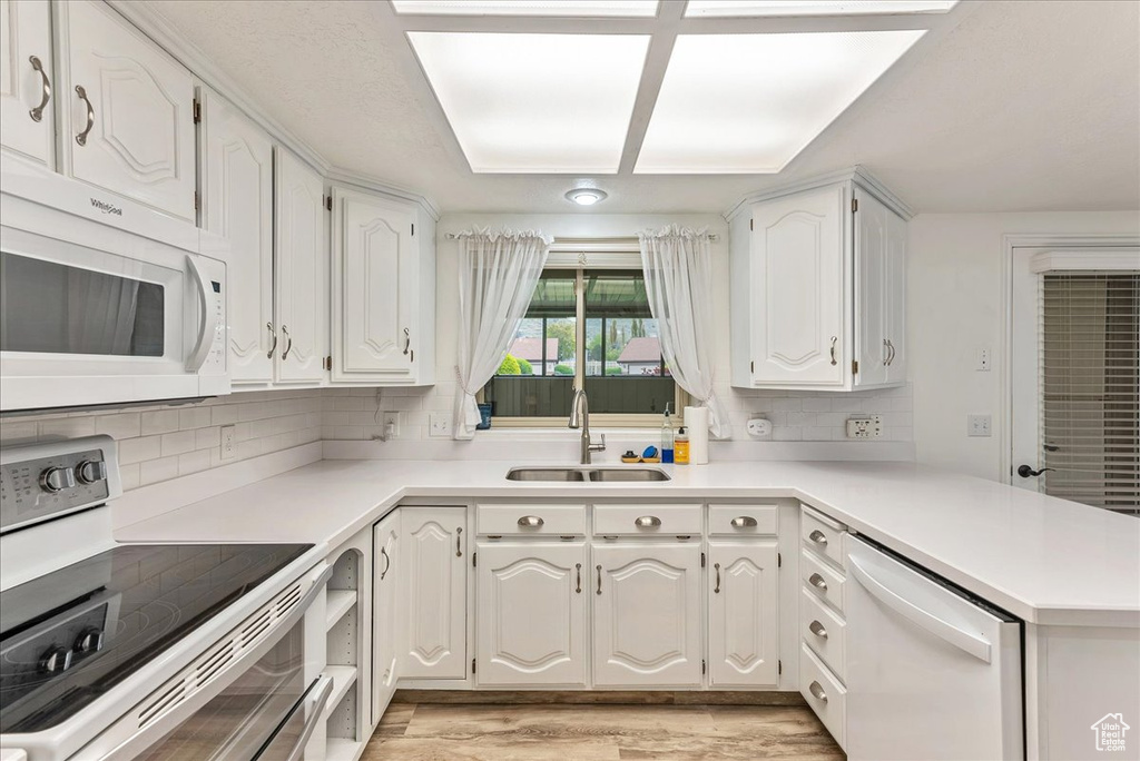 Kitchen featuring white cabinets, white appliances, light wood-type flooring, sink, and tasteful backsplash
