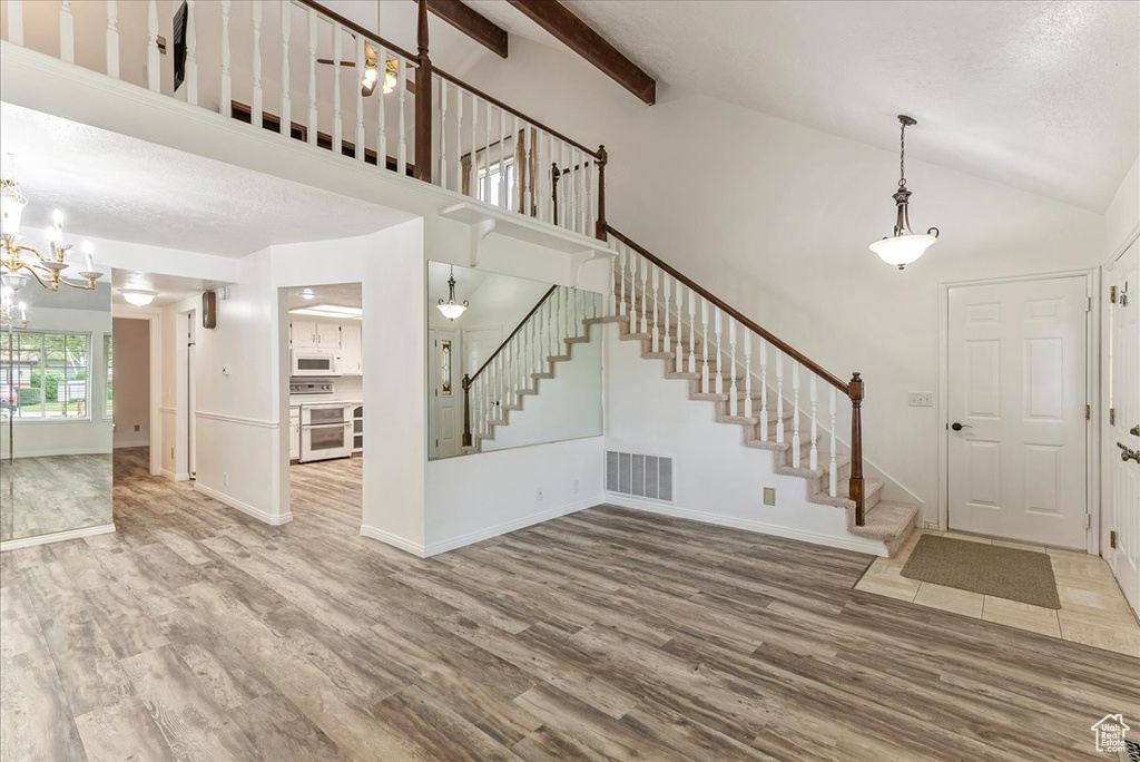 Foyer entrance featuring hardwood / wood-style flooring, beam ceiling, high vaulted ceiling, and a notable chandelier