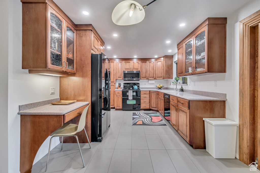 Kitchen with black refrigerator, light tile flooring, light stone counters, and range