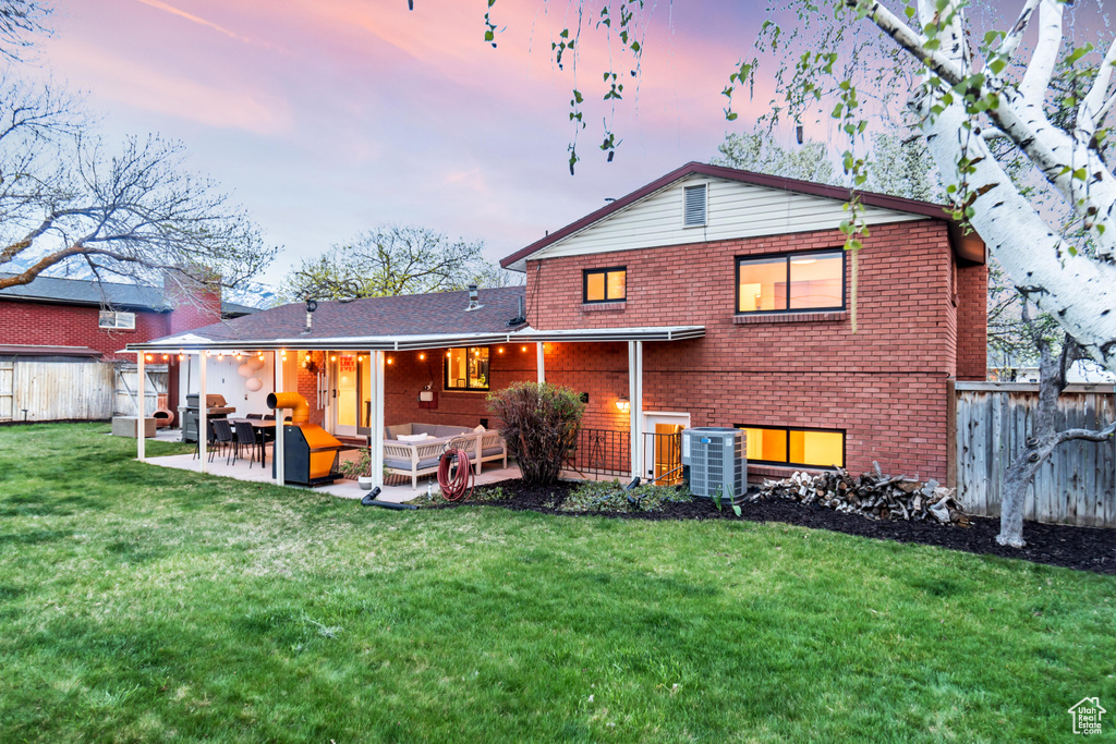 Back house at dusk featuring a patio area, outdoor lounge area, a lawn, and central AC unit