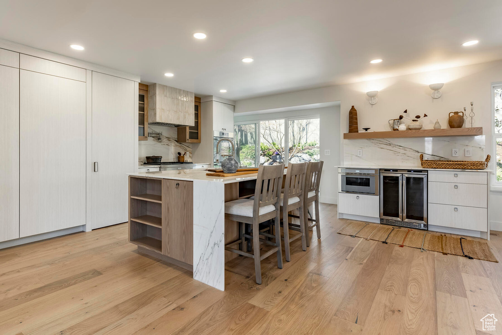Kitchen featuring backsplash, a breakfast bar area, light hardwood / wood-style floors, wine cooler, and white cabinetry