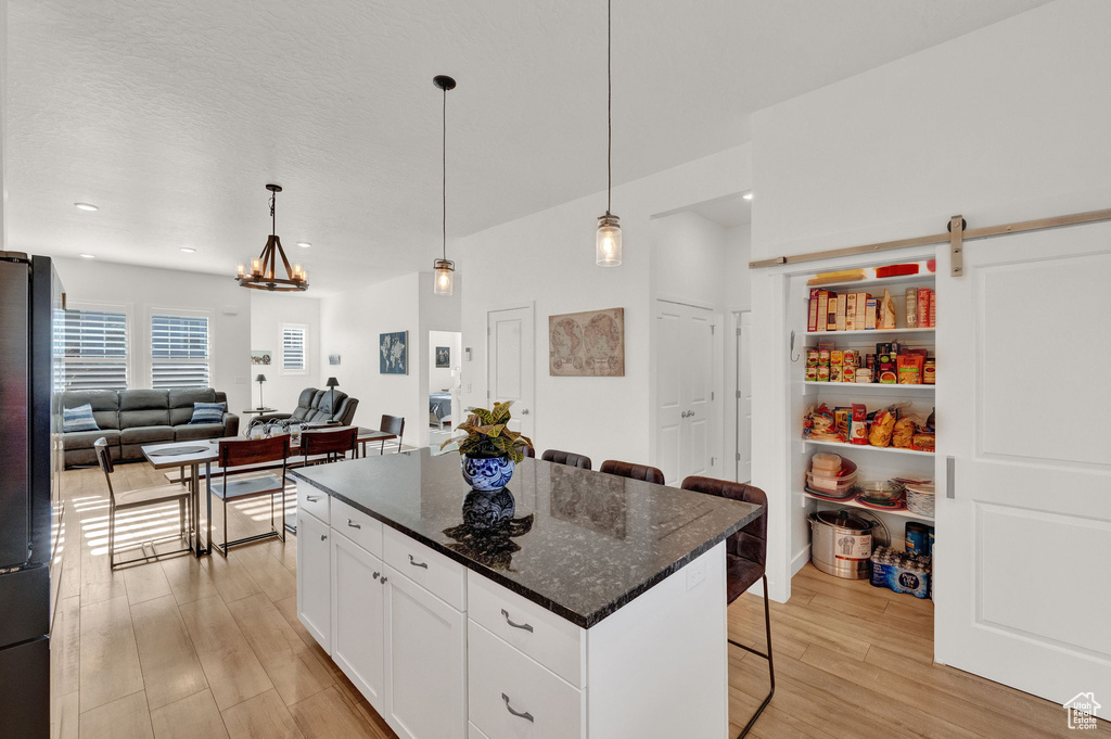 Kitchen featuring pendant lighting, a kitchen island, white cabinets, light wood-type flooring, and a kitchen breakfast bar