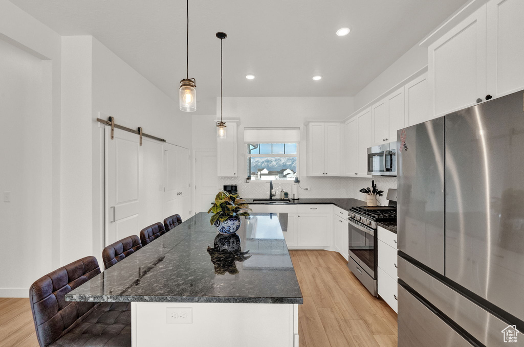 Kitchen featuring pendant lighting, light wood-type flooring, appliances with stainless steel finishes, a kitchen bar, and a kitchen island
