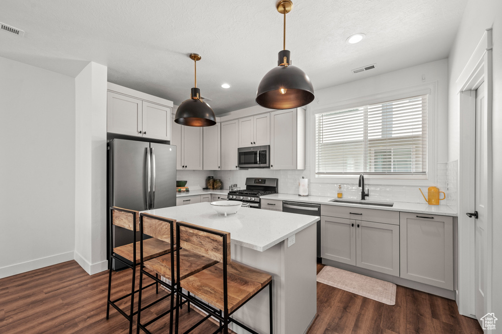 Kitchen with appliances with stainless steel finishes, a kitchen island, sink, dark hardwood / wood-style flooring, and pendant lighting