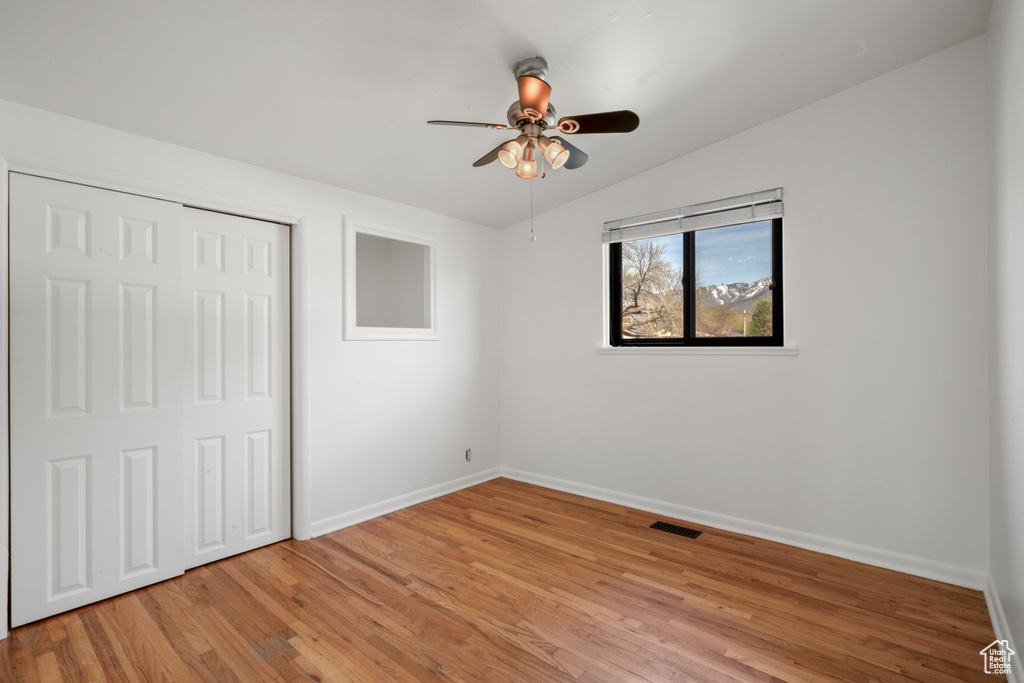 Unfurnished bedroom with a closet, ceiling fan, vaulted ceiling, and light wood-type flooring