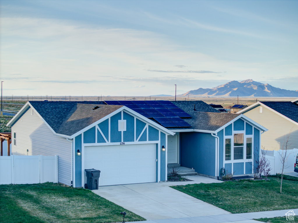 Single story home featuring solar panels, a mountain view, a garage, and a front lawn