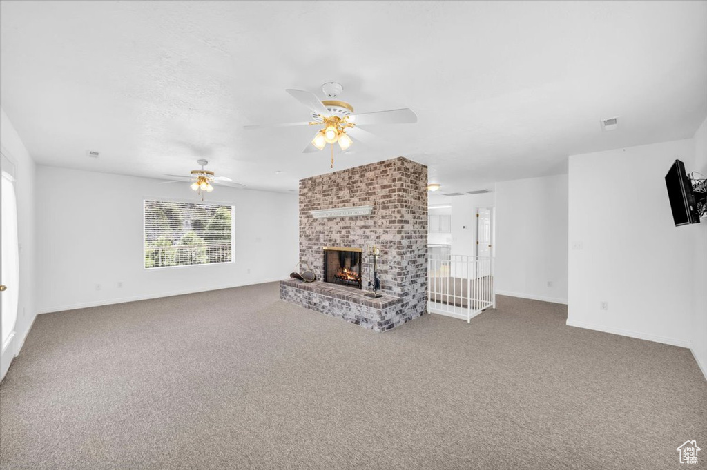 Unfurnished living room featuring brick wall, ceiling fan, a brick fireplace, and dark colored carpet