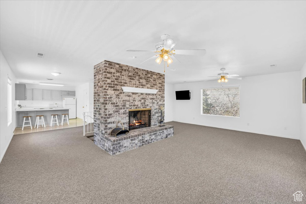 Unfurnished living room featuring brick wall, light carpet, ceiling fan, and a fireplace