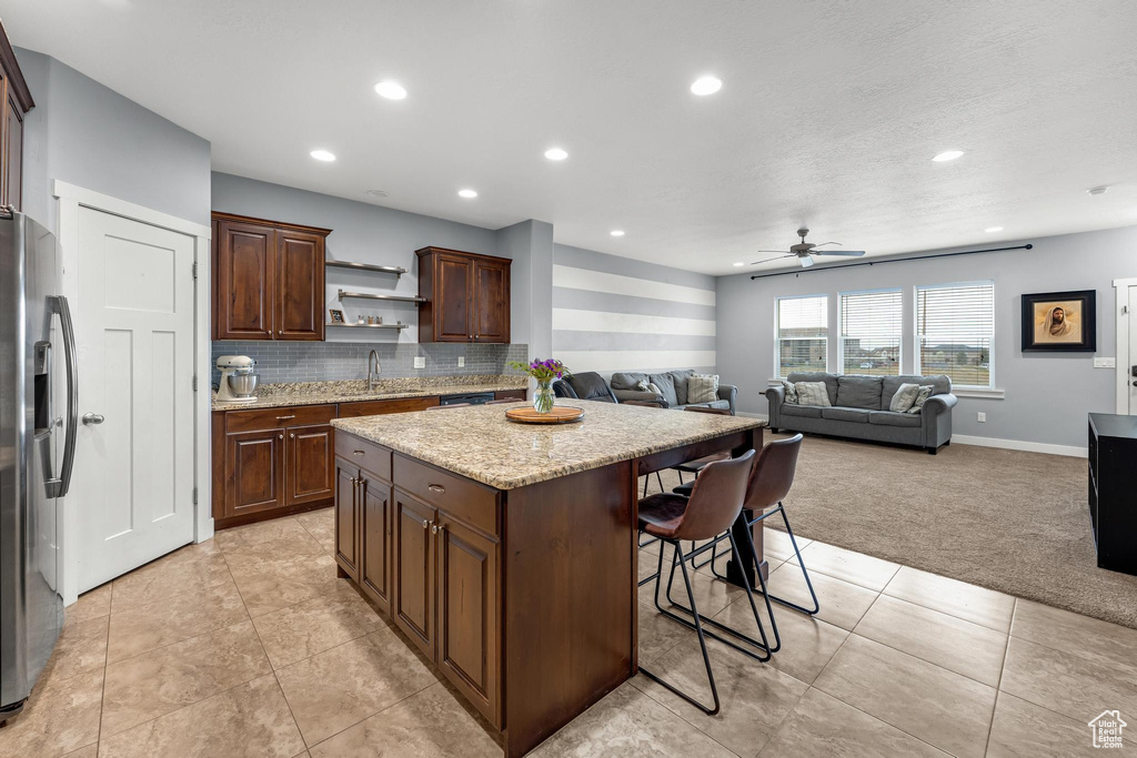Kitchen with a center island, stainless steel refrigerator with ice dispenser, light tile floors, a breakfast bar area, and tasteful backsplash
