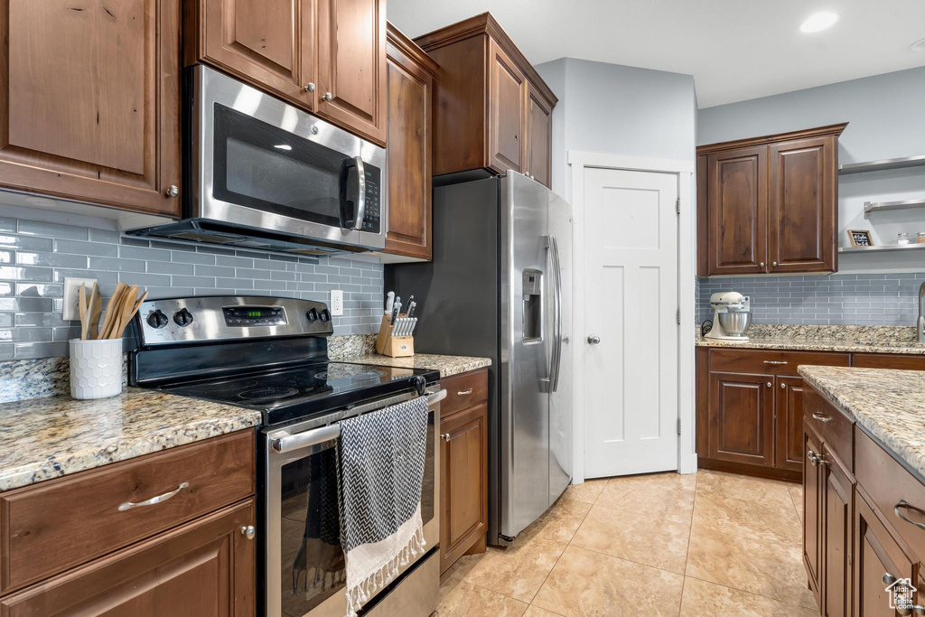 Kitchen featuring appliances with stainless steel finishes, tasteful backsplash, light stone countertops, and light tile flooring
