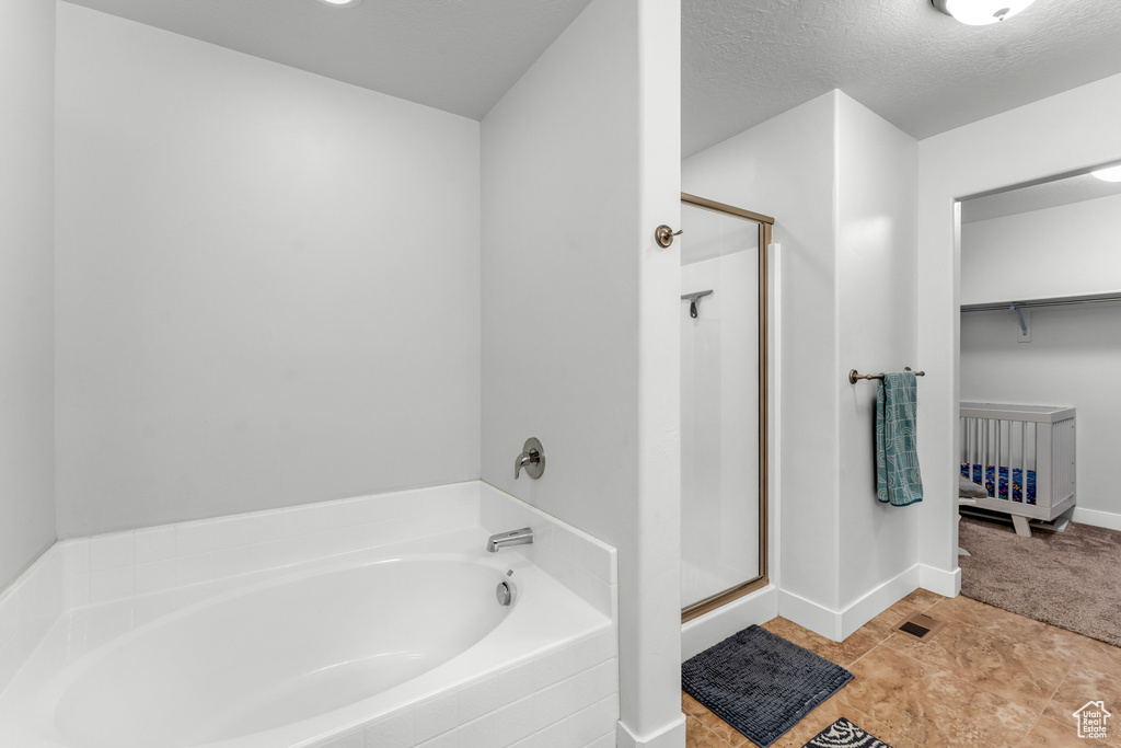 Bathroom with tile flooring, independent shower and bath, and a textured ceiling