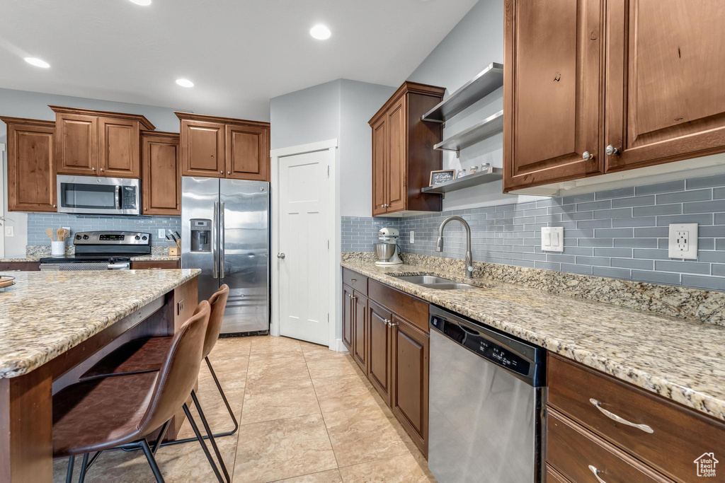 Kitchen featuring backsplash, sink, stainless steel appliances, and light stone countertops