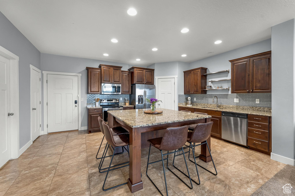 Kitchen featuring appliances with stainless steel finishes, light stone countertops, light tile flooring, and a breakfast bar