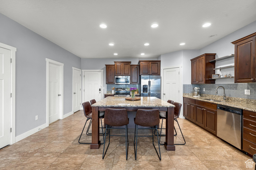 Kitchen with a kitchen breakfast bar, appliances with stainless steel finishes, light stone counters, a kitchen island, and tasteful backsplash