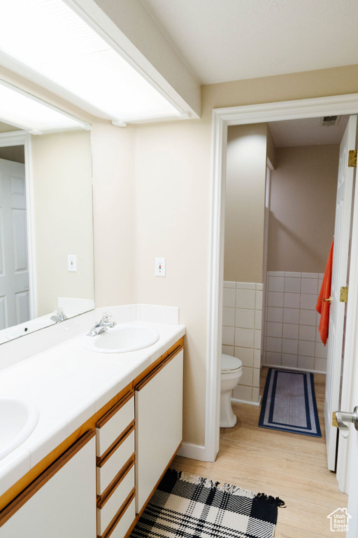 Bathroom with dual vanity, tile walls, hardwood / wood-style flooring, and toilet