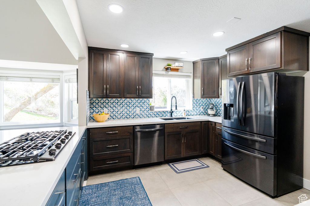 Kitchen featuring dark brown cabinetry, light tile floors, sink, tasteful backsplash, and stainless steel appliances