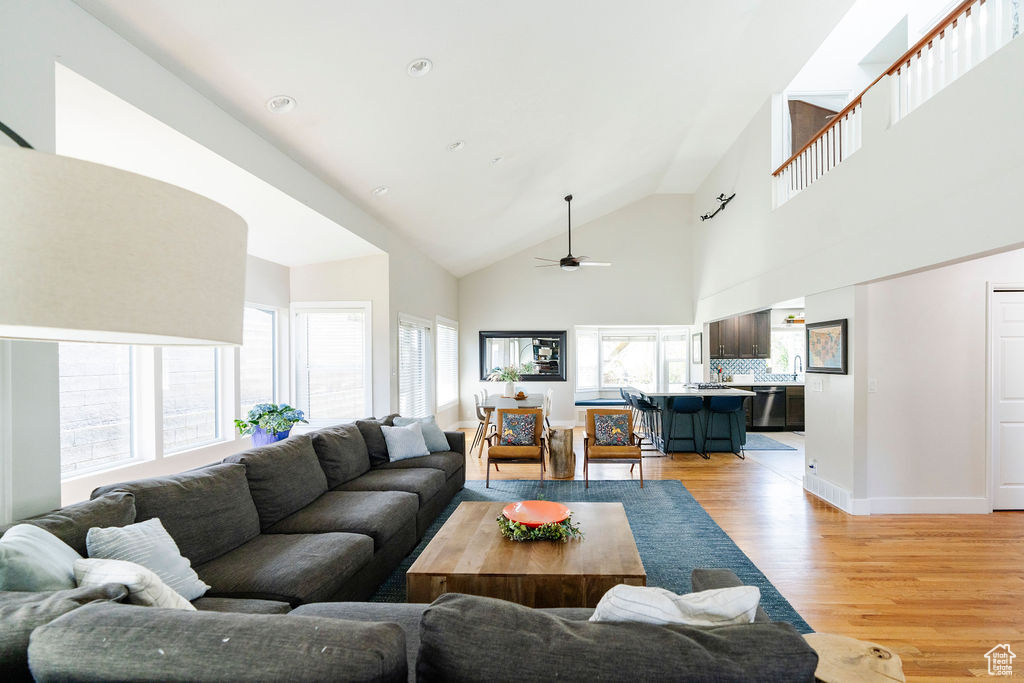 Living room featuring high vaulted ceiling, ceiling fan, and light wood-type flooring