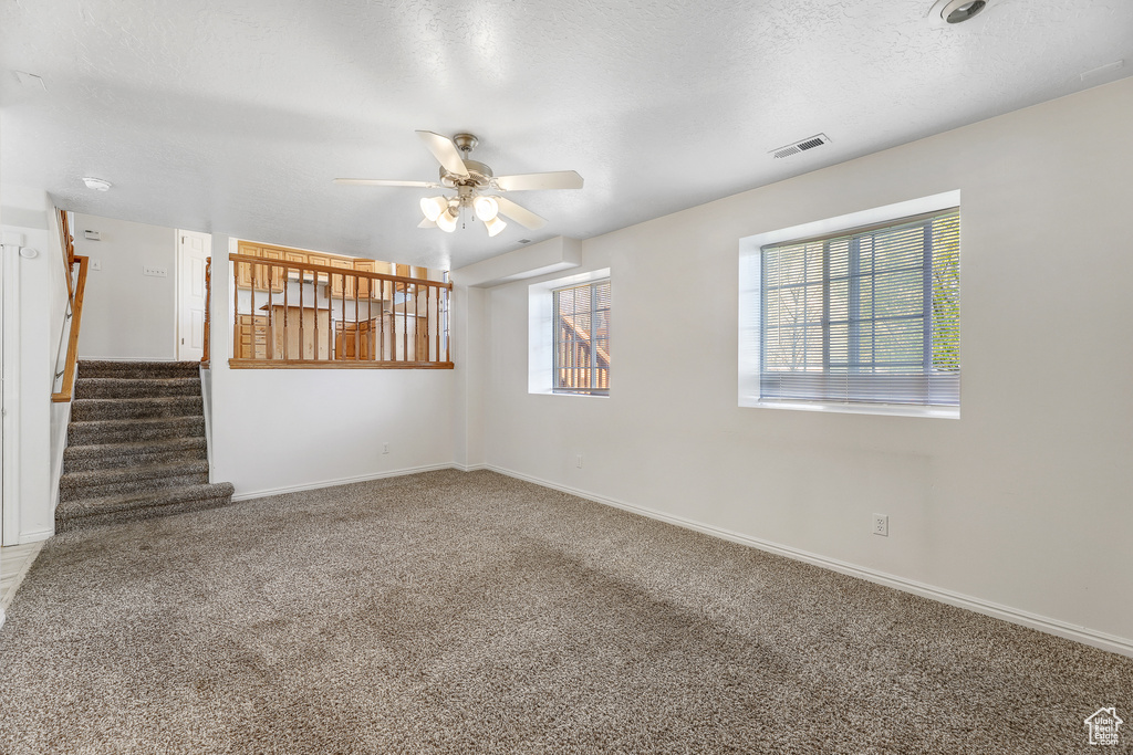 Interior space with a textured ceiling, a wealth of natural light, ceiling fan, and carpet
