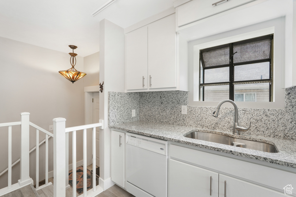 Kitchen with light stone counters, dishwasher, tasteful backsplash, light wood-type flooring, and hanging light fixtures