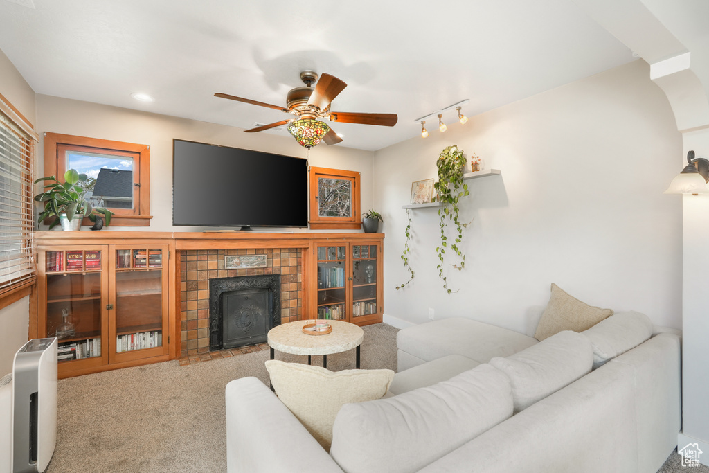 Living room featuring light colored carpet, ceiling fan, track lighting, and a tile fireplace