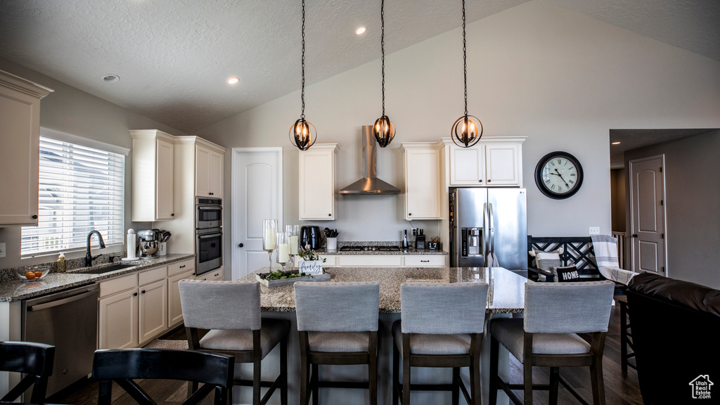 Kitchen featuring hanging light fixtures, a kitchen island, stainless steel appliances, wall chimney exhaust hood, and sink