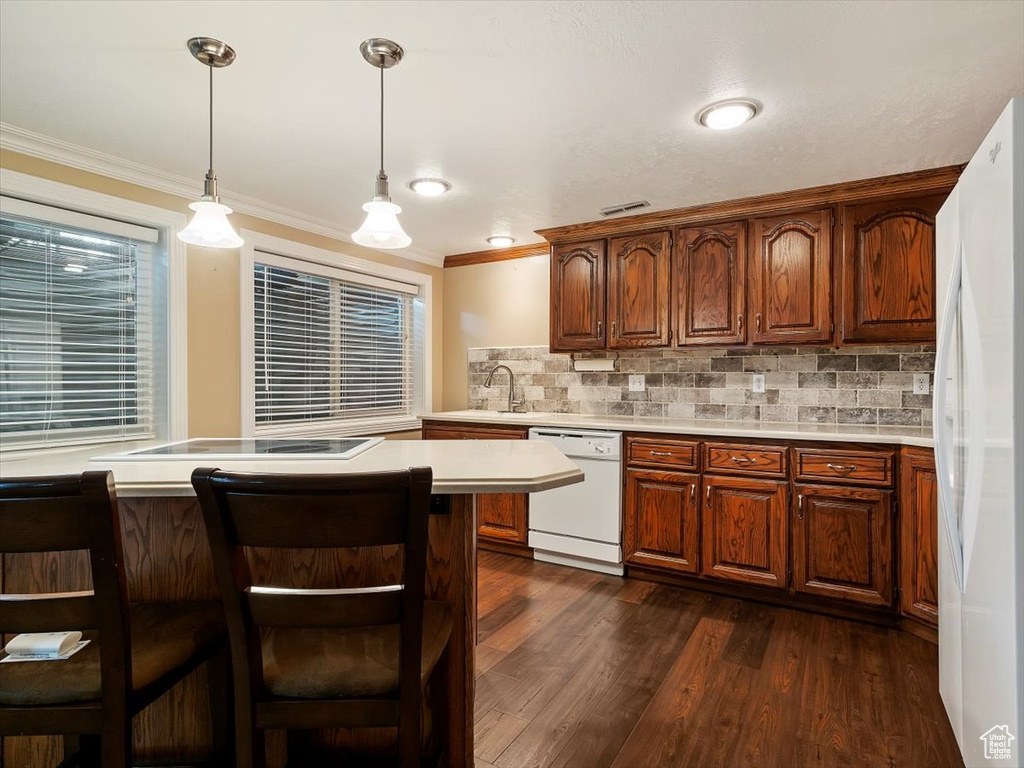 Kitchen with backsplash, dark hardwood / wood-style floors, white appliances, and pendant lighting