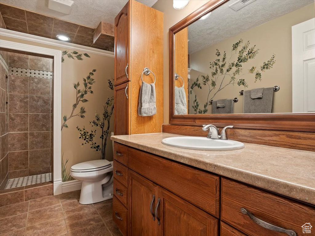 Bathroom featuring vanity with extensive cabinet space, tile floors, a tile shower, toilet, and a textured ceiling