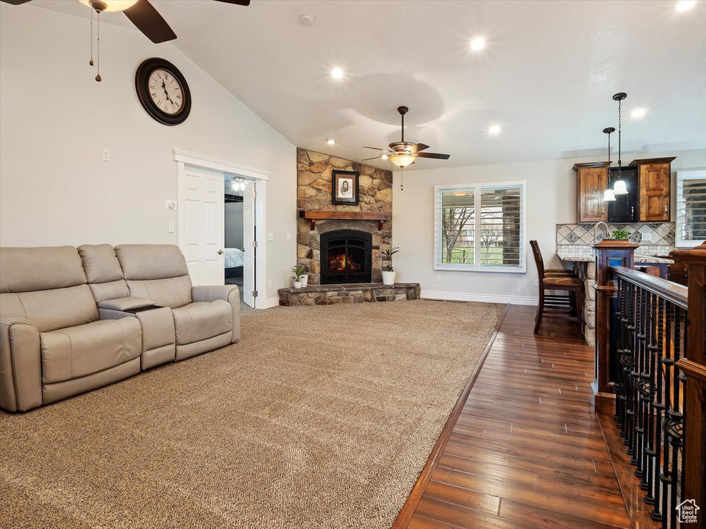 Living room with a fireplace, dark colored carpet, sink, ceiling fan, and lofted ceiling