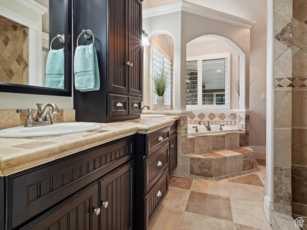 Bathroom featuring vanity, a relaxing tiled bath, tile floors, and crown molding
