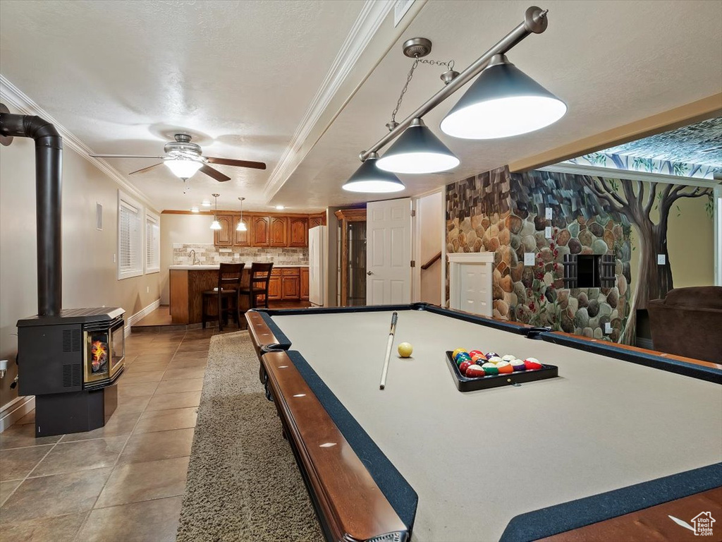 Rec room featuring a wood stove, ornamental molding, pool table, light tile floors, and ceiling fan