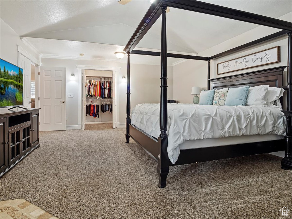 Carpeted bedroom with a closet, vaulted ceiling, a walk in closet, and ornamental molding