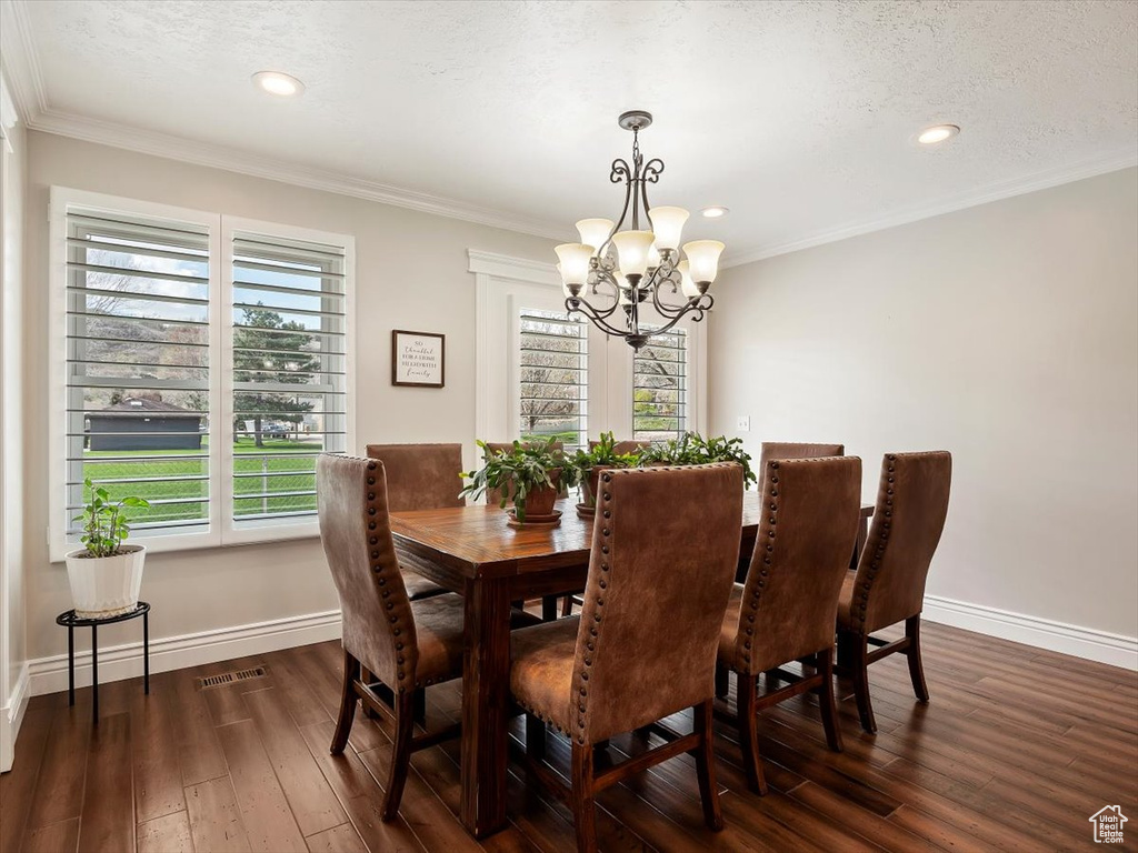 Dining room featuring a textured ceiling, dark hardwood / wood-style flooring, crown molding, and a chandelier