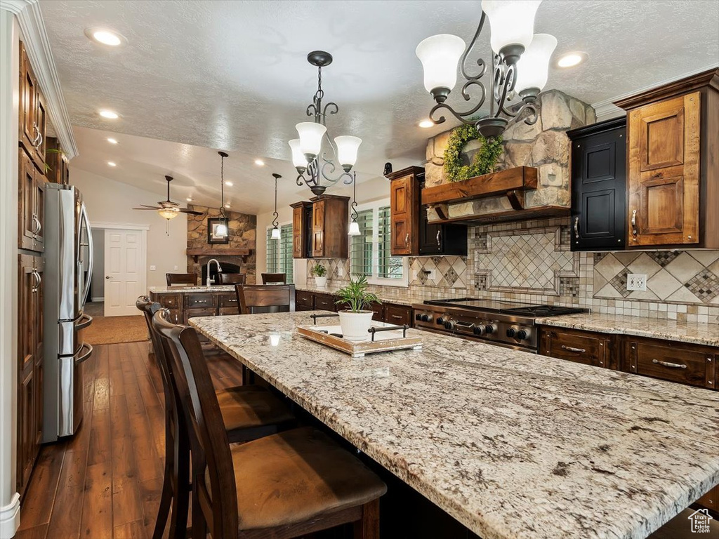 Kitchen featuring a center island with sink, stainless steel fridge, ceiling fan with notable chandelier, and pendant lighting