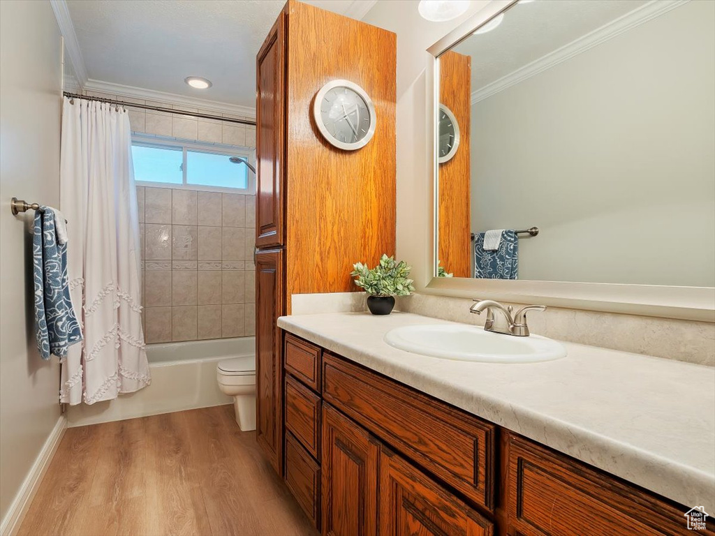 Full bathroom featuring vanity with extensive cabinet space, shower / bath combination with curtain, toilet, ornamental molding, and hardwood / wood-style flooring