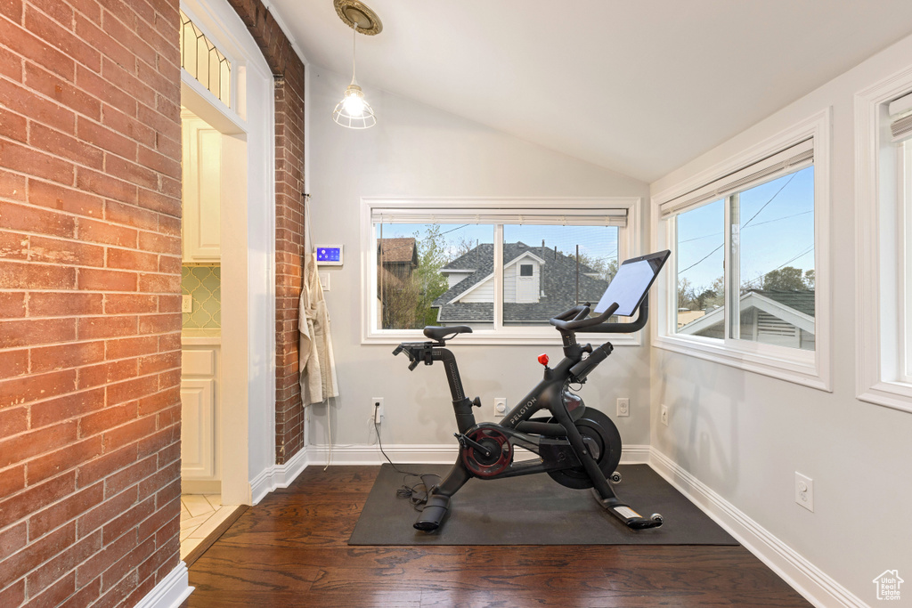 Workout room with brick wall, dark wood-type flooring, and vaulted ceiling