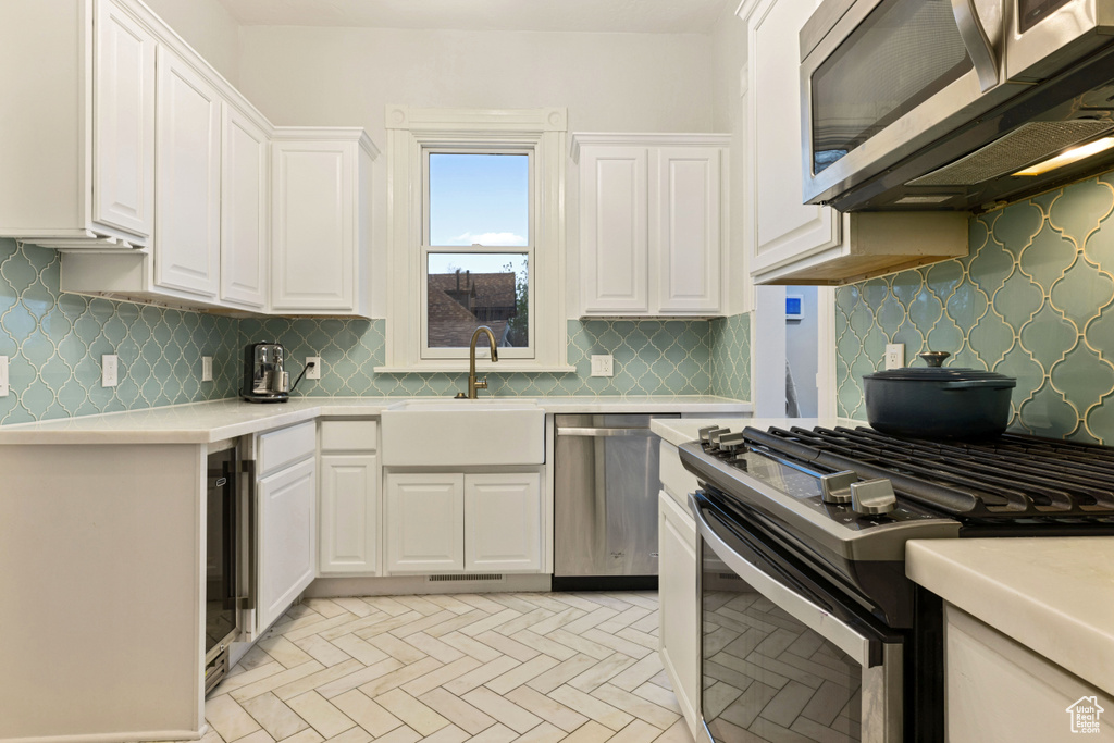 Kitchen with stainless steel appliances, tasteful backsplash, wine cooler, white cabinets, and sink