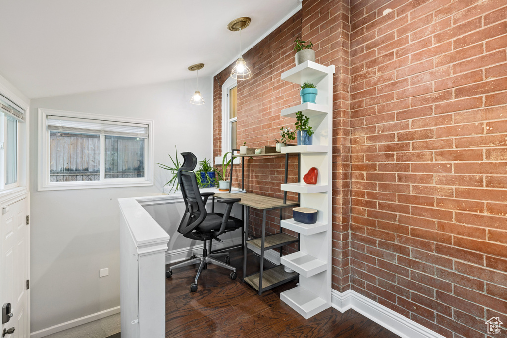 Home office with lofted ceiling, brick wall, and dark wood-type flooring
