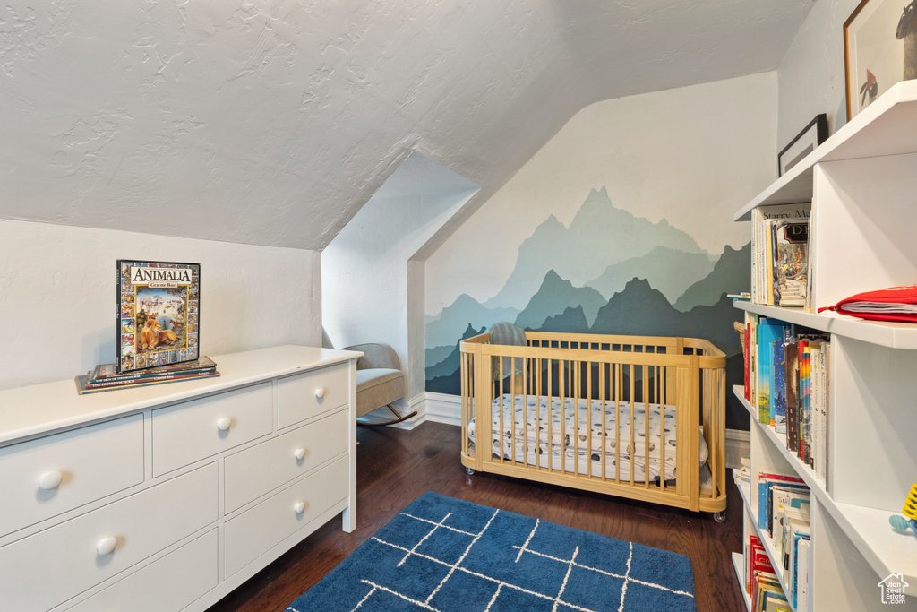 Bedroom featuring dark hardwood / wood-style floors, lofted ceiling, and a nursery area