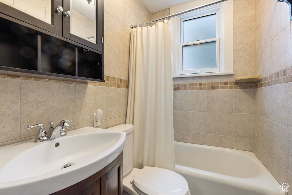 Full bathroom featuring tile walls, shower / tub combo with curtain, oversized vanity, tasteful backsplash, and toilet