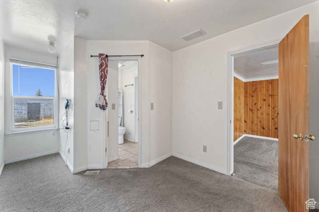 Unfurnished bedroom with wooden walls, connected bathroom, and light carpet