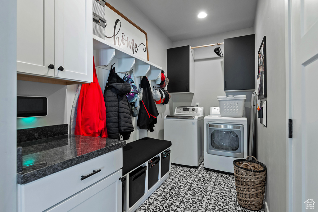 Clothes washing area with cabinets, light tile floors, and washer and clothes dryer