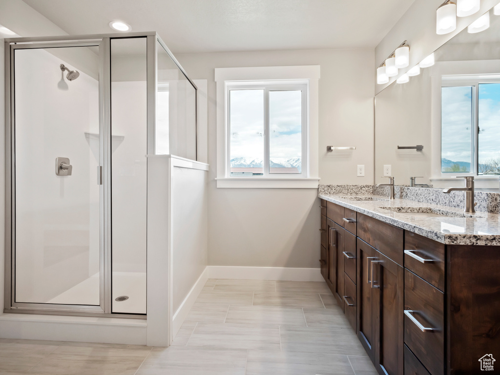 Bathroom with a wealth of natural light, double sink, a shower with shower door, and vanity with extensive cabinet space