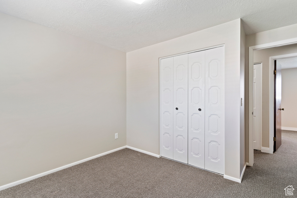 Unfurnished bedroom featuring a closet, dark carpet, and a textured ceiling