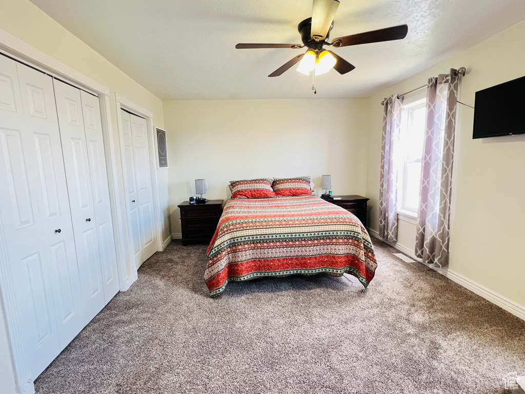 Bedroom featuring dark colored carpet, ceiling fan, and multiple closets