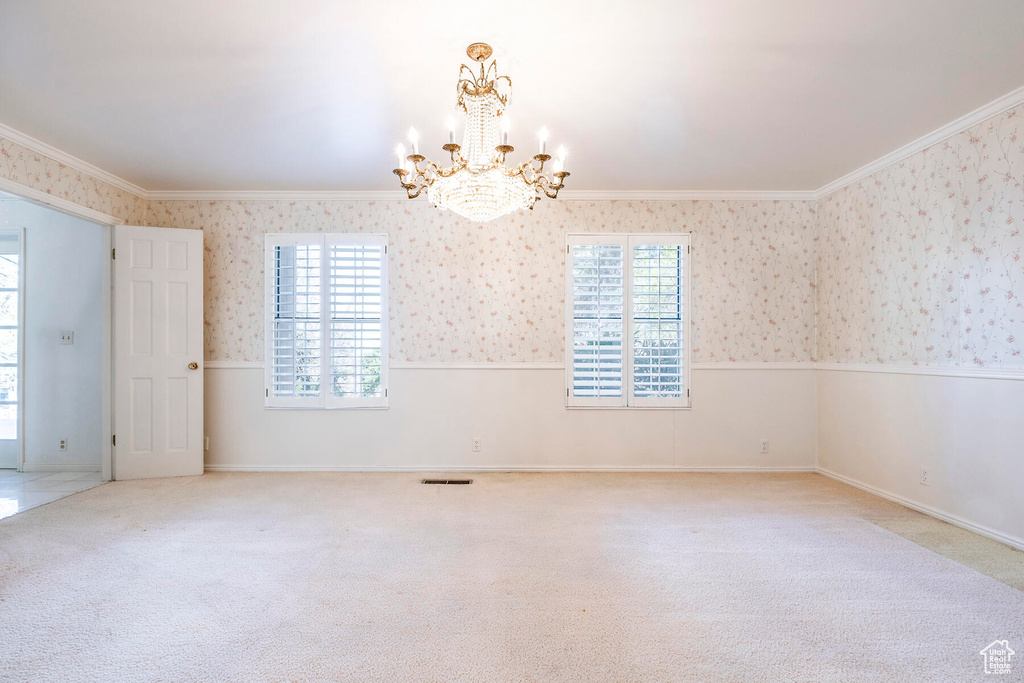 Carpeted empty room featuring crown molding and a notable chandelier
