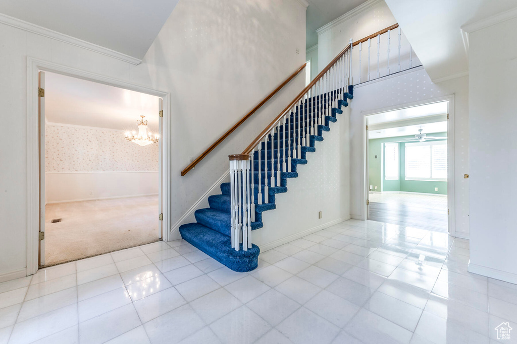 Stairs with an inviting chandelier, light tile floors, and ornamental molding